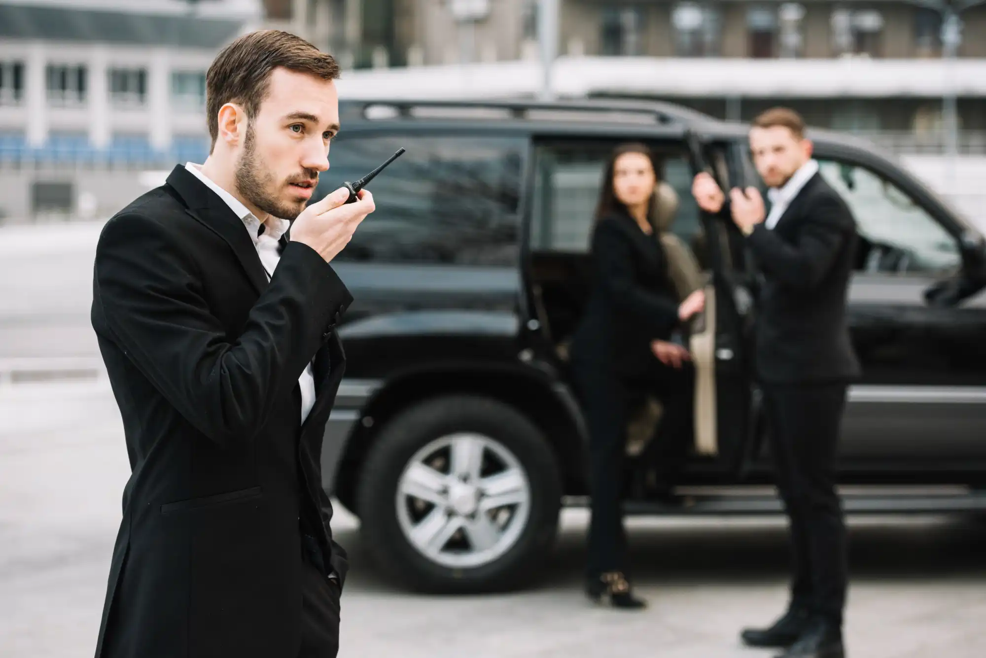 Close protection officer coordinating by radio beside a client vehicle